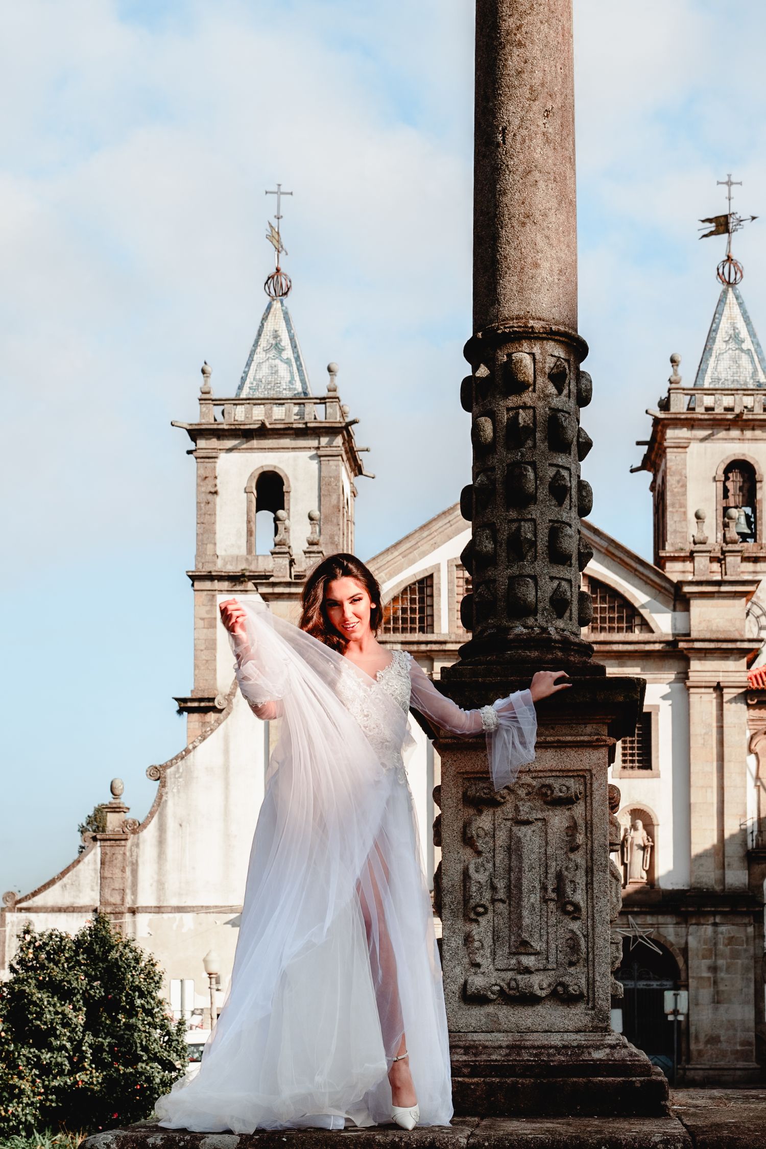 Bride in flowing white dress poses elegantly in front of a historic church with twin bell towers.