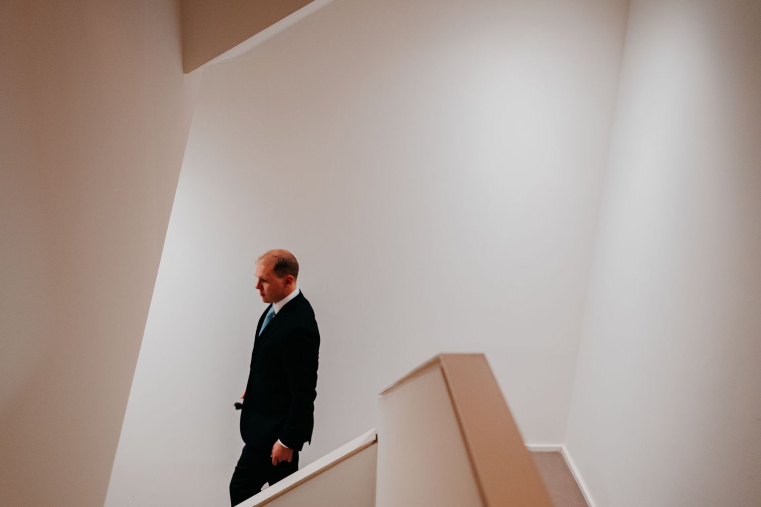 A businessman in a dark suit walks up white minimalist stairs in a modern building.