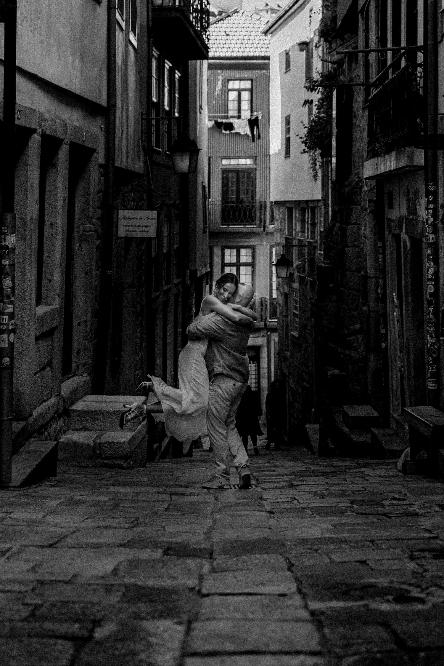 A romantic embrace captured in black and white on cobblestone streets between historic buildings.