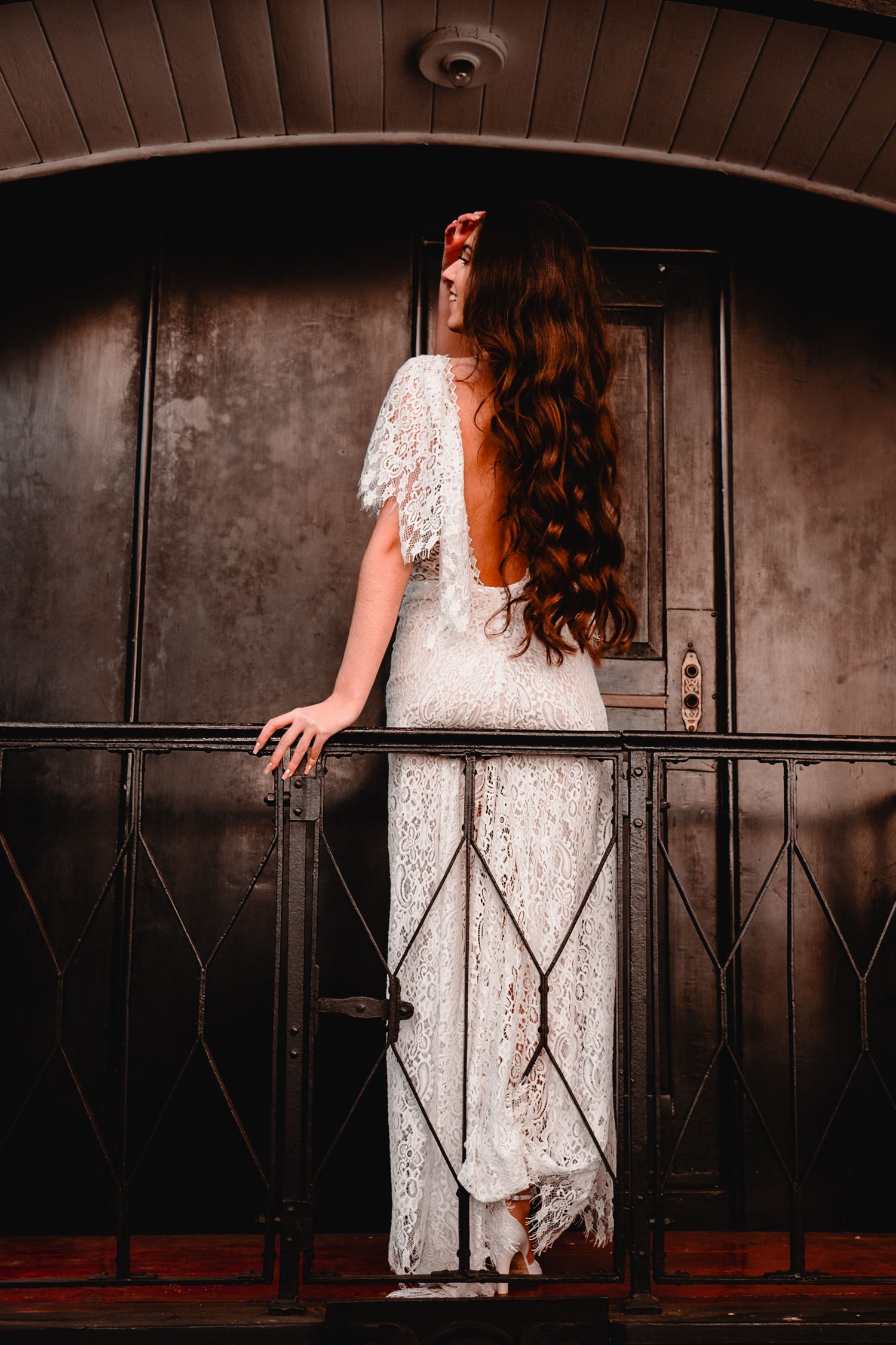 A figure in a white lace dress stands dramatically against a dark railing in vintage-style photography.