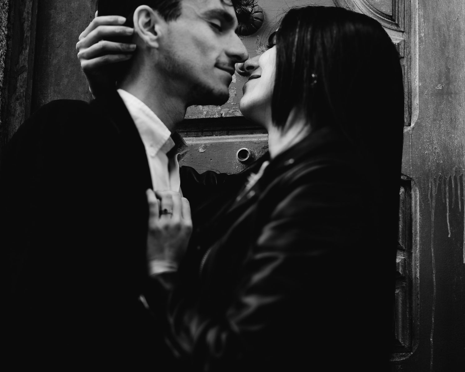 Black and white romantic couple almost kissing near vintage door in intimate close-up portrait photo.