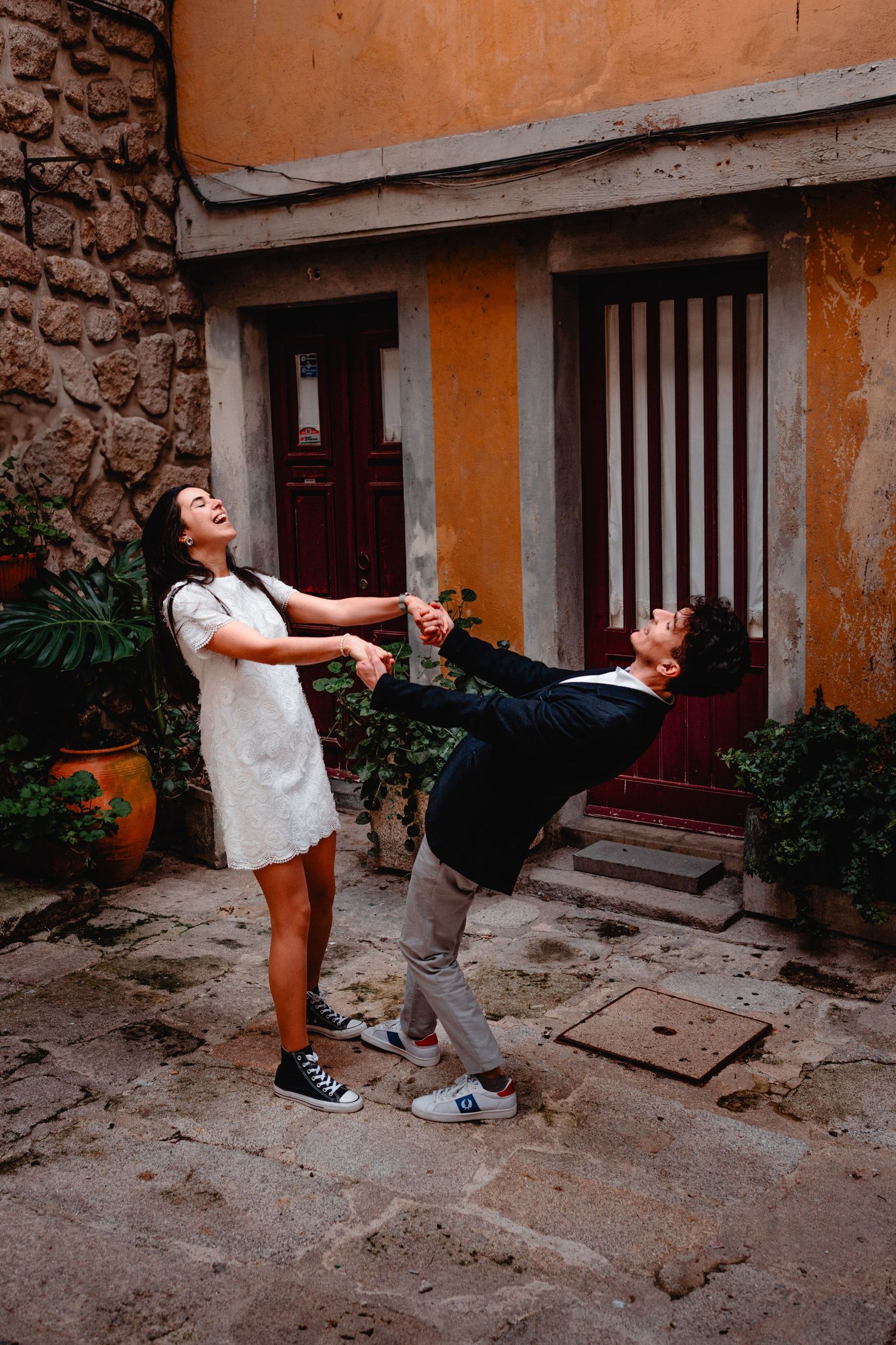 Joyful couple playfully dancing and laughing together in a charming rustic European courtyard.
