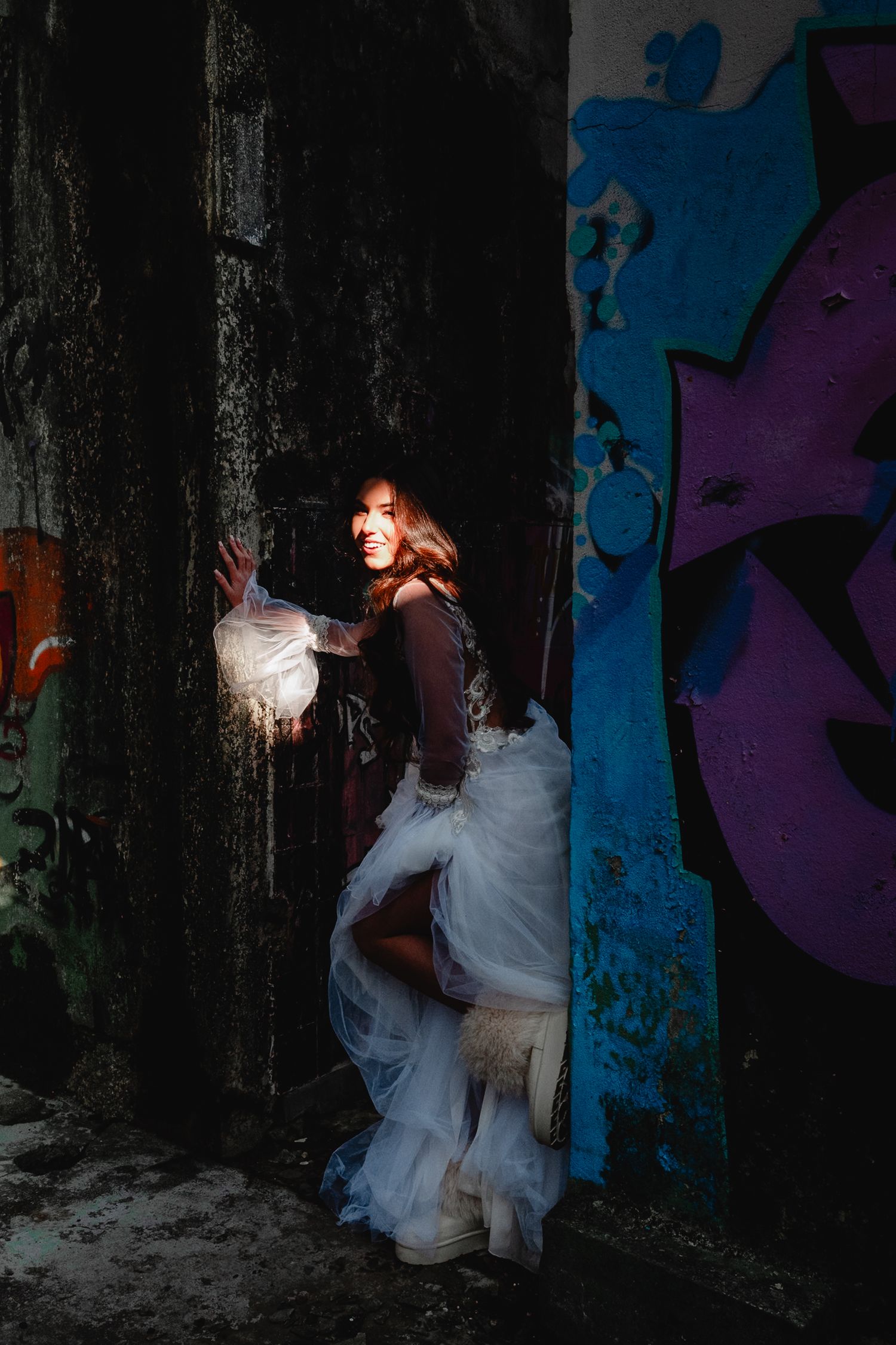 Dramatic bridal portrait with urban graffiti backdrop and contrasting lighting.