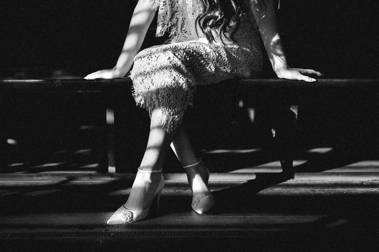 Woman wearing a white lace dress and heels posing on dark train tracks at night.