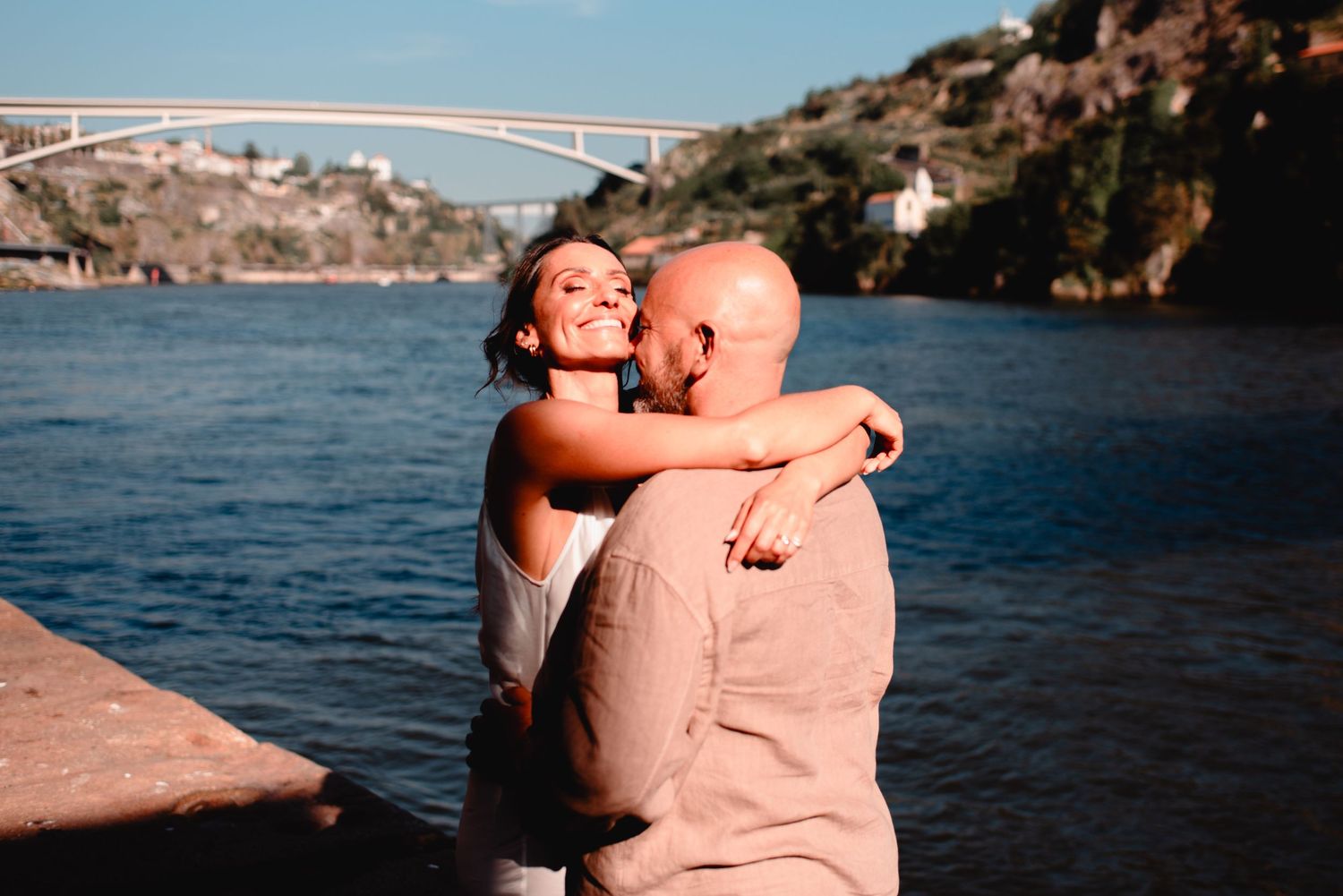 Intimate embrace captured against coastal cityscape backdrop during sunset.