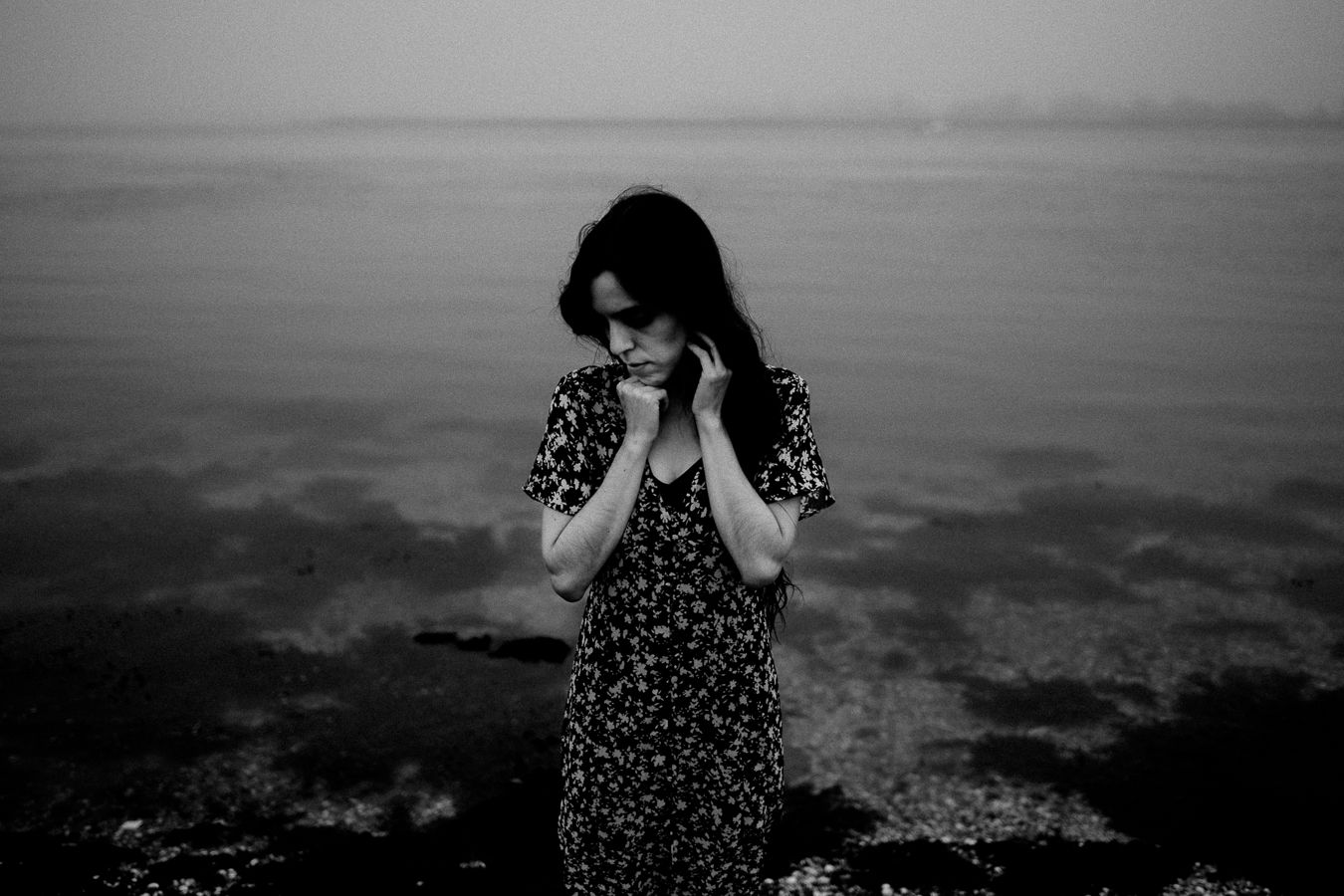 Emotional black and white photograph of someone in a patterned dress by the water.