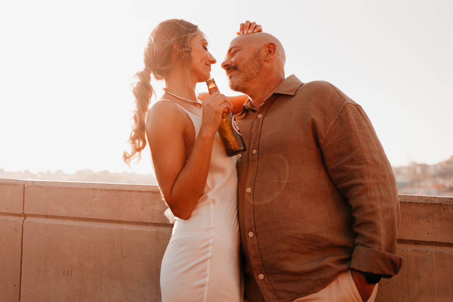 Elderly man and young woman share a romantic moment on a rooftop terrace at sunset.