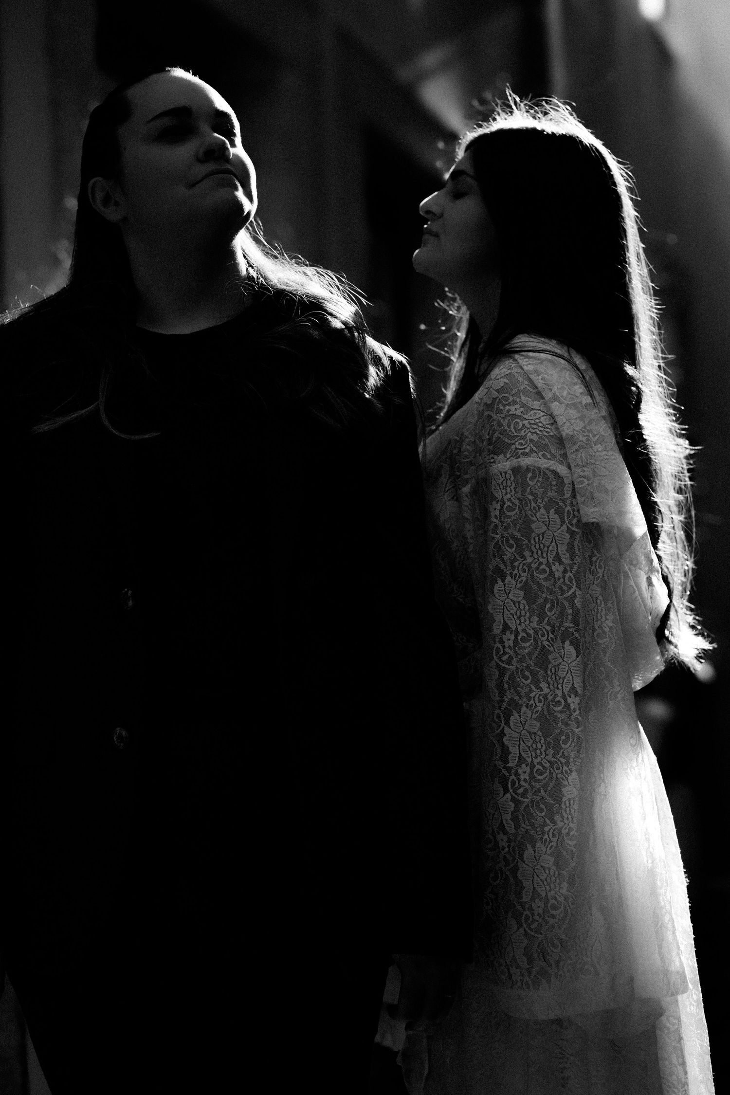 Black and white photo of two women with long dark hair standing close together in dramatic lighting.