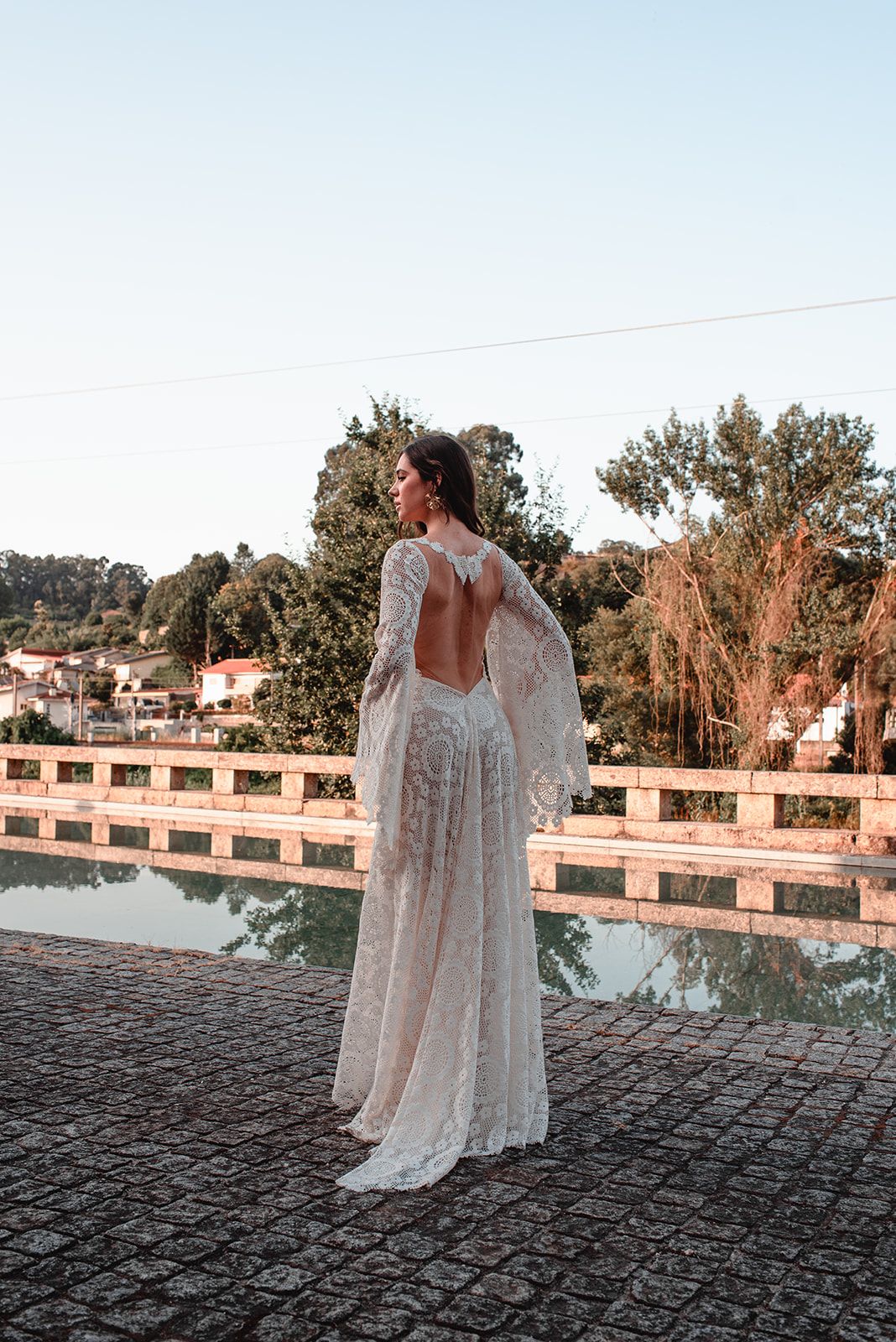 Backless lace wedding dress captured at sunset on stone terrace with scenic backdrop.