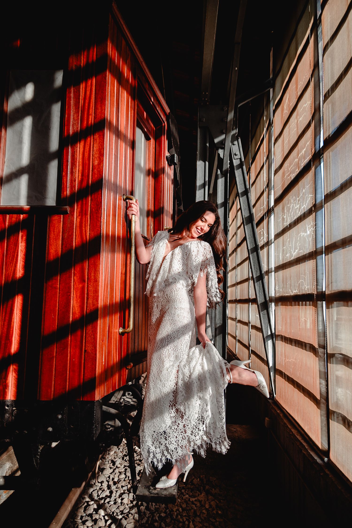 Artistic bridal fashion photography with dramatic red lighting and shadows on wooden walls.