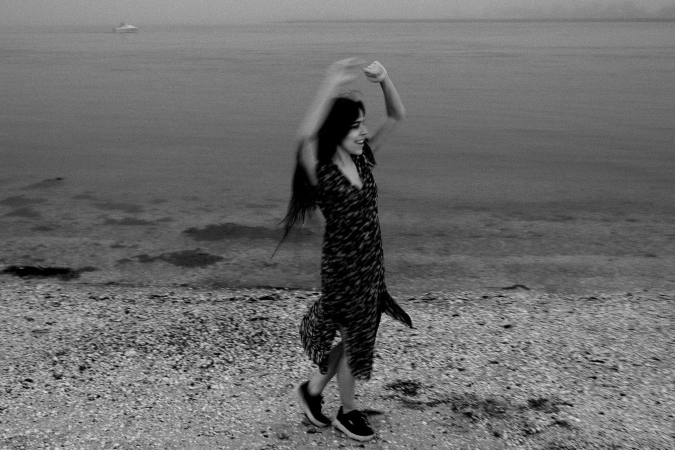 Dynamic black and white photo of someone twirling in a dress by the shore.