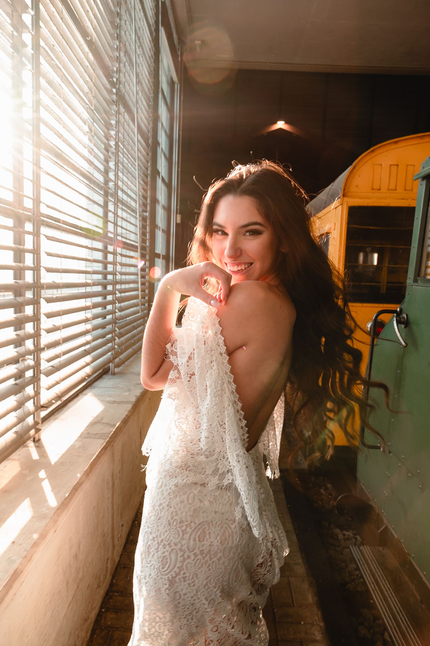 Light streams through window blinds creating dramatic shadows on figure in white lace dress.