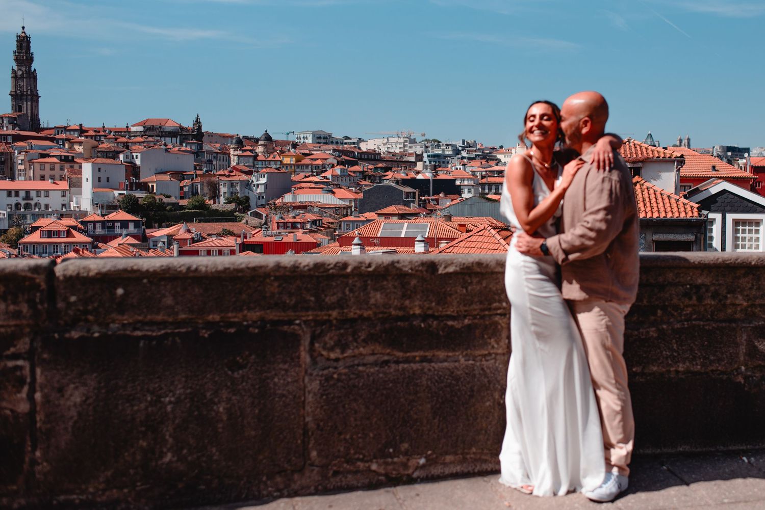 Romantic couple embracing against a panoramic cityscape with terracotta rooftops and blue sky in Porto, Portugal.