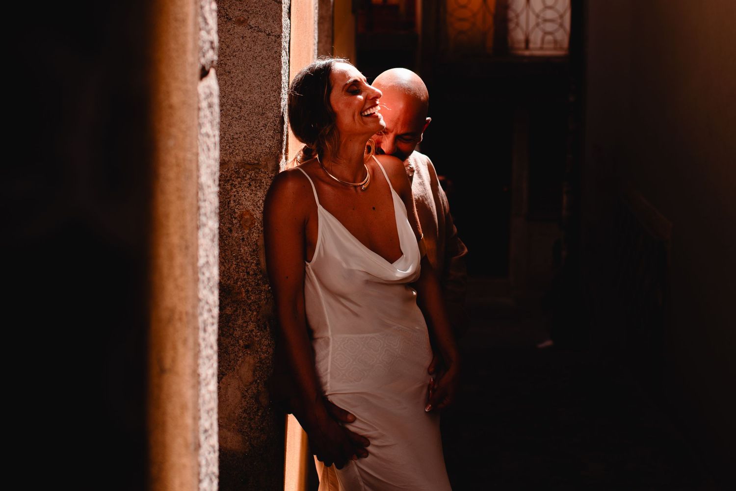 A couple sharing an intimate moment in a sunlit narrow alleyway.