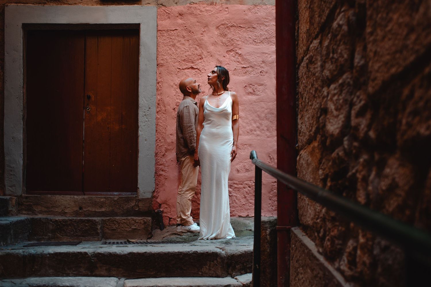 Two figures stand in romantic pose against pink stone walls and stairs.