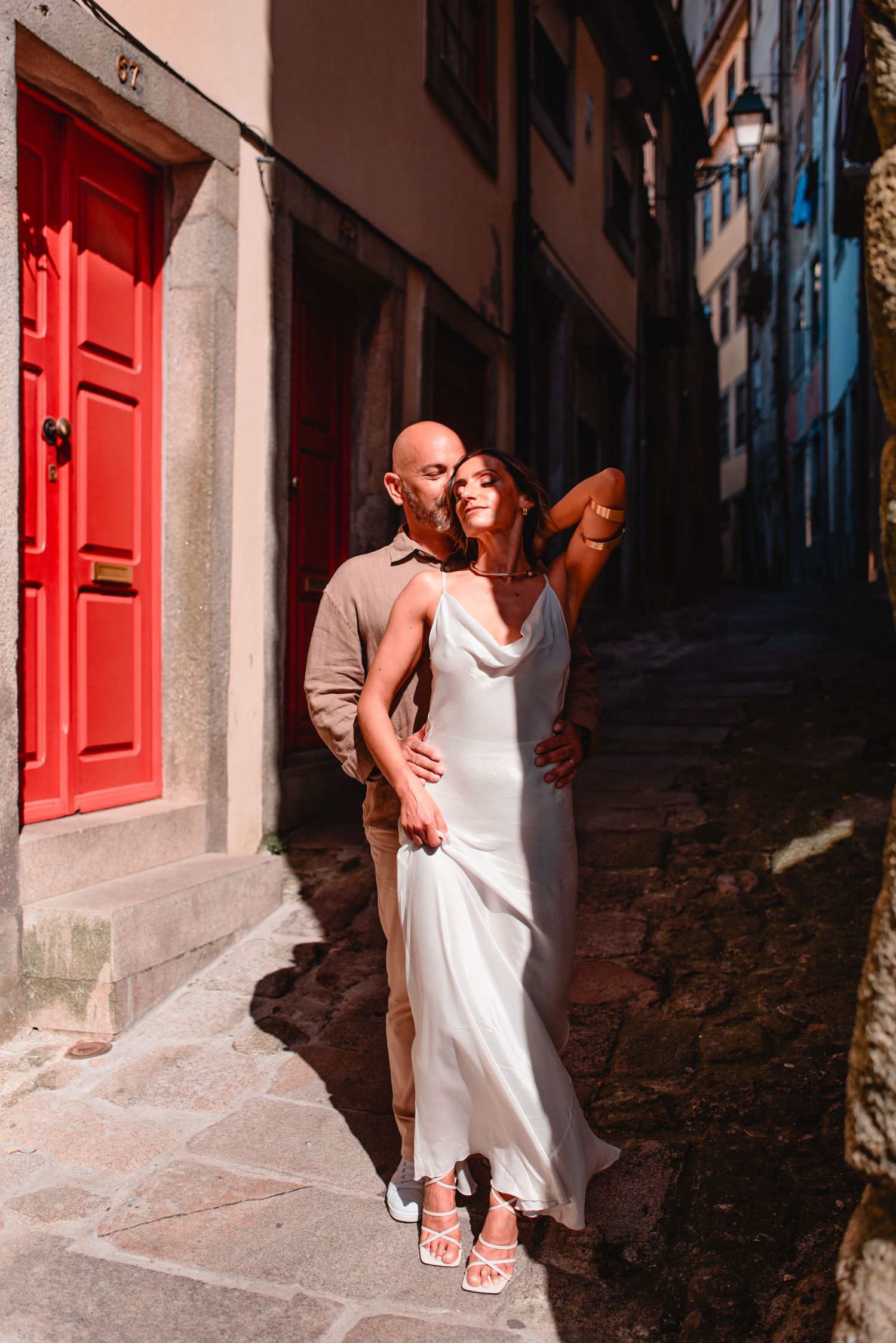 A couple embraces in a narrow European alleyway with stone walls and a bright red door.