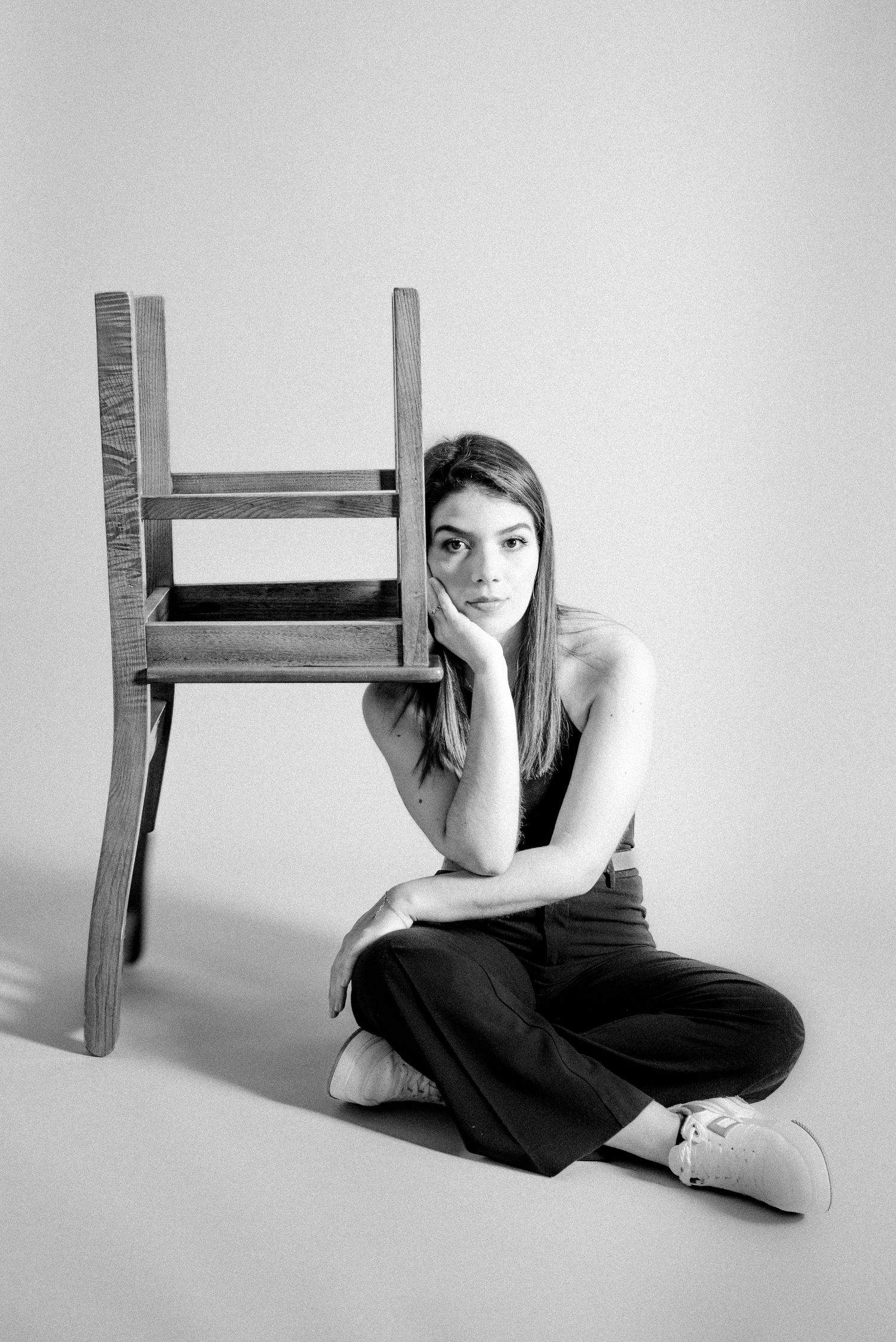 Artistic black and white portrait with wooden chair in minimalist studio setting.