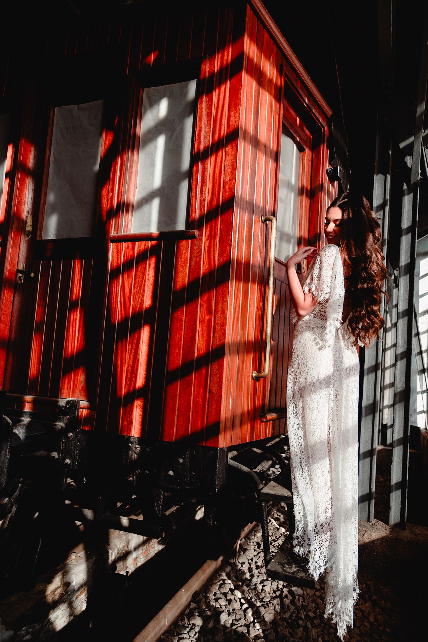 Dramatic fashion photography with red lighting, shadows and white dress against wooden architecture.