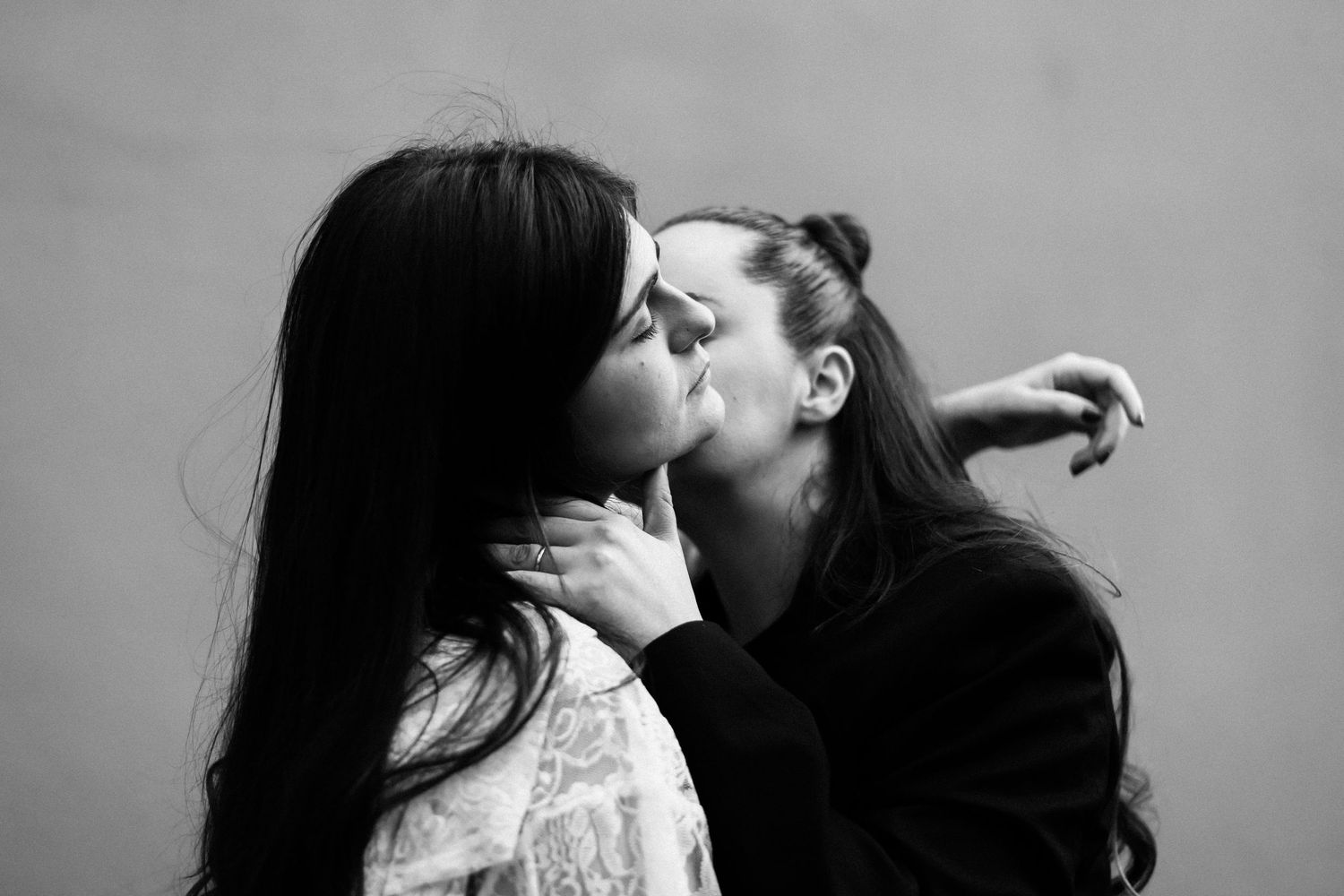 Black and white photo of two women sharing an intimate kiss, one gently holding the other's neck.