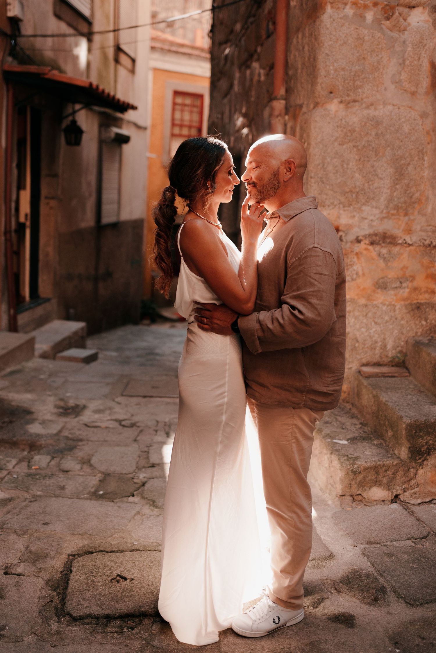 Couple in wedding attire sharing a romantic moment in a charming cobblestone alley with rustic stone walls.