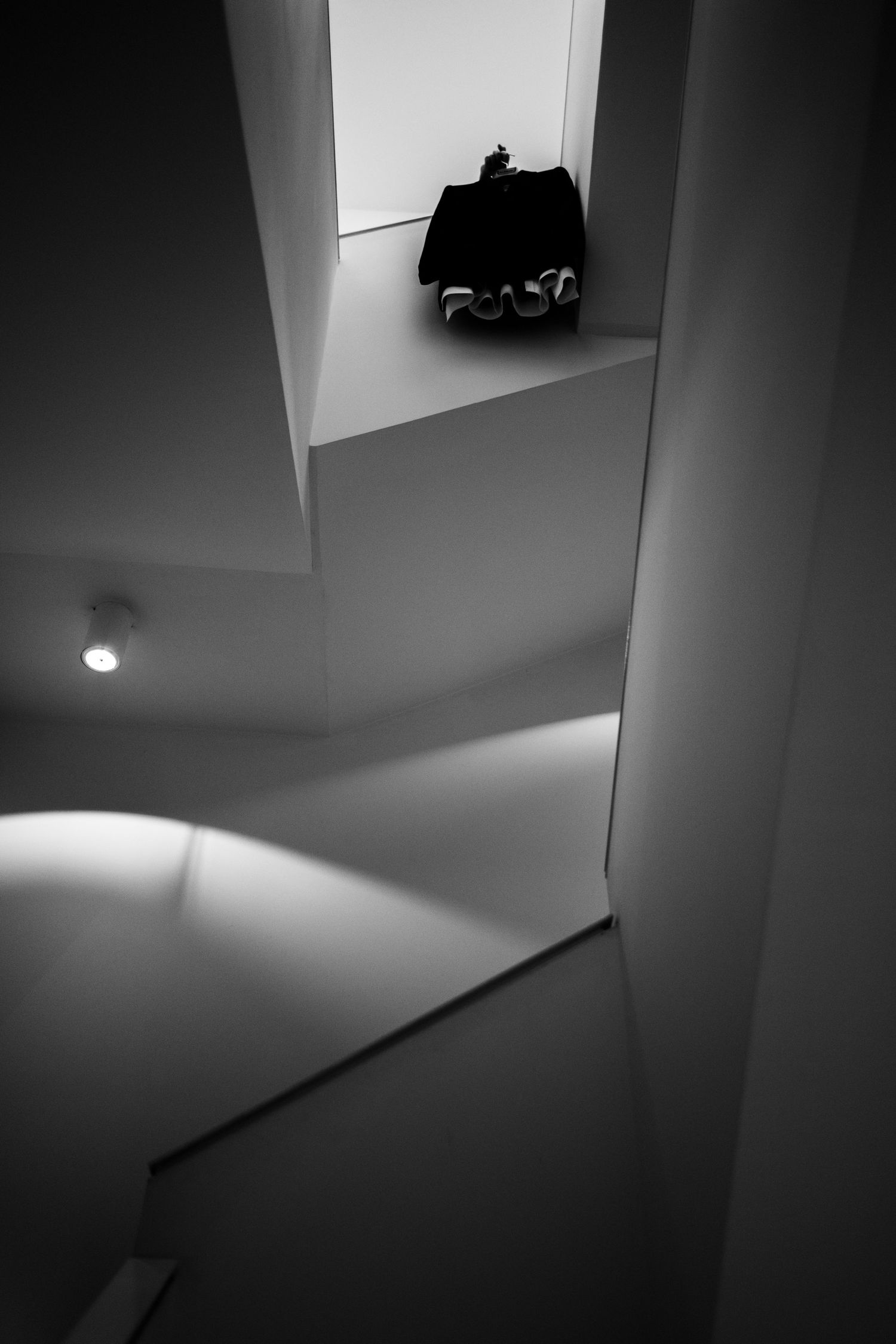 Black and white interior architectural photo featuring geometric walls, a spotlight, and a dark sculpture on a white ledge.