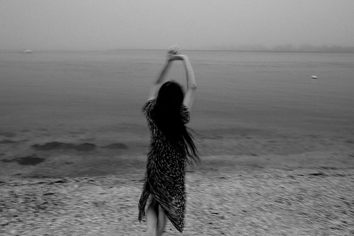 Silhouette of a person in a flowing dress dancing on a beach at twilight.