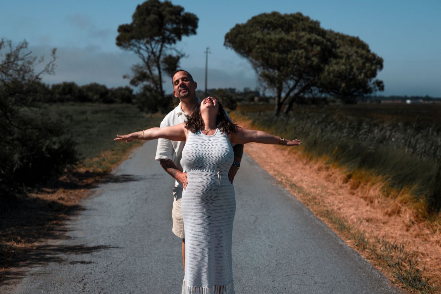 A couple walks along a scenic waterfront path surrounded by nature.
