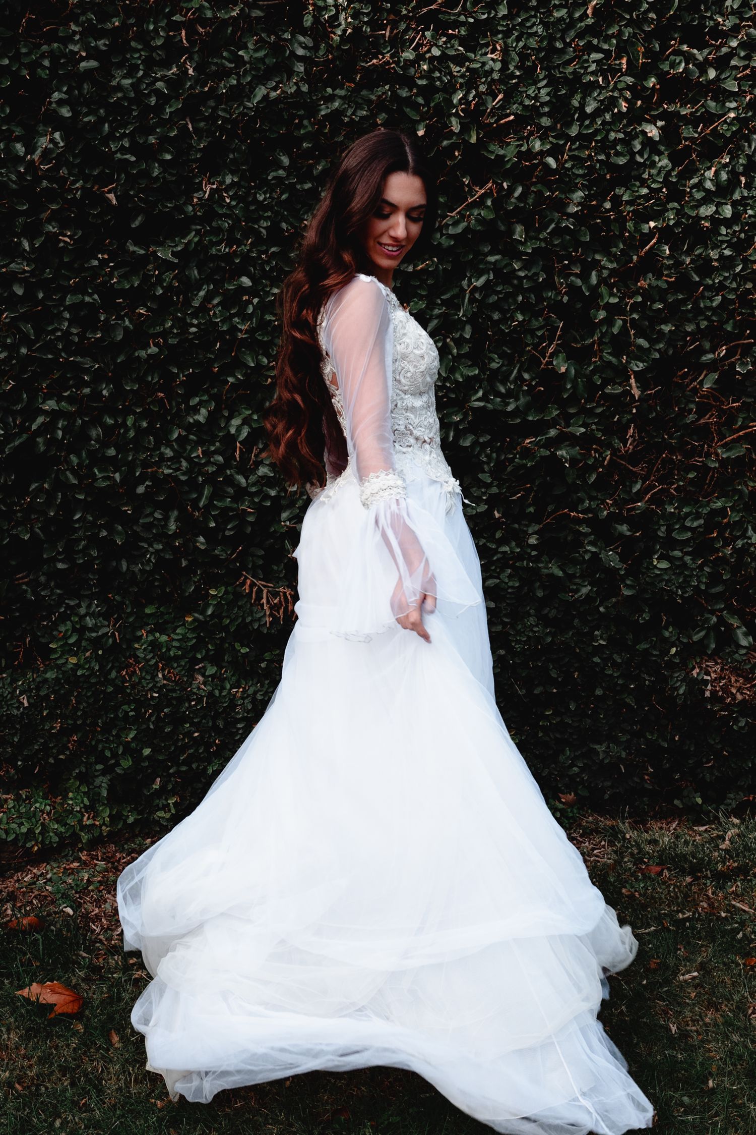 Elegant wedding gown with lace details photographed against ivy wall.