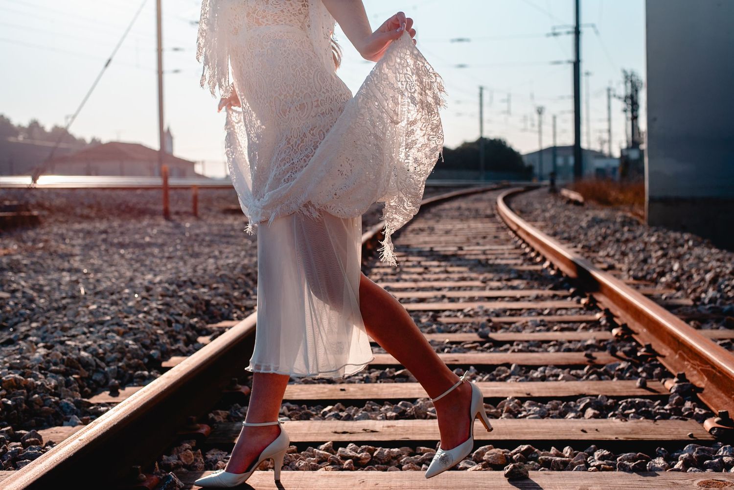 Person in white dress walking along railroad tracks at sunset casting long shadows.