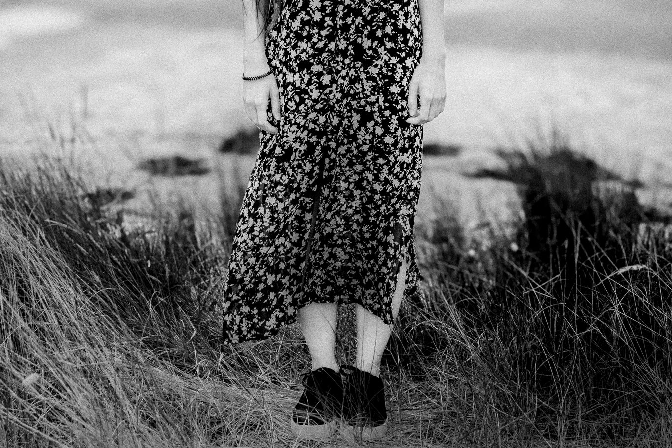 Black and white image of floral dress and boots standing in tall grass.