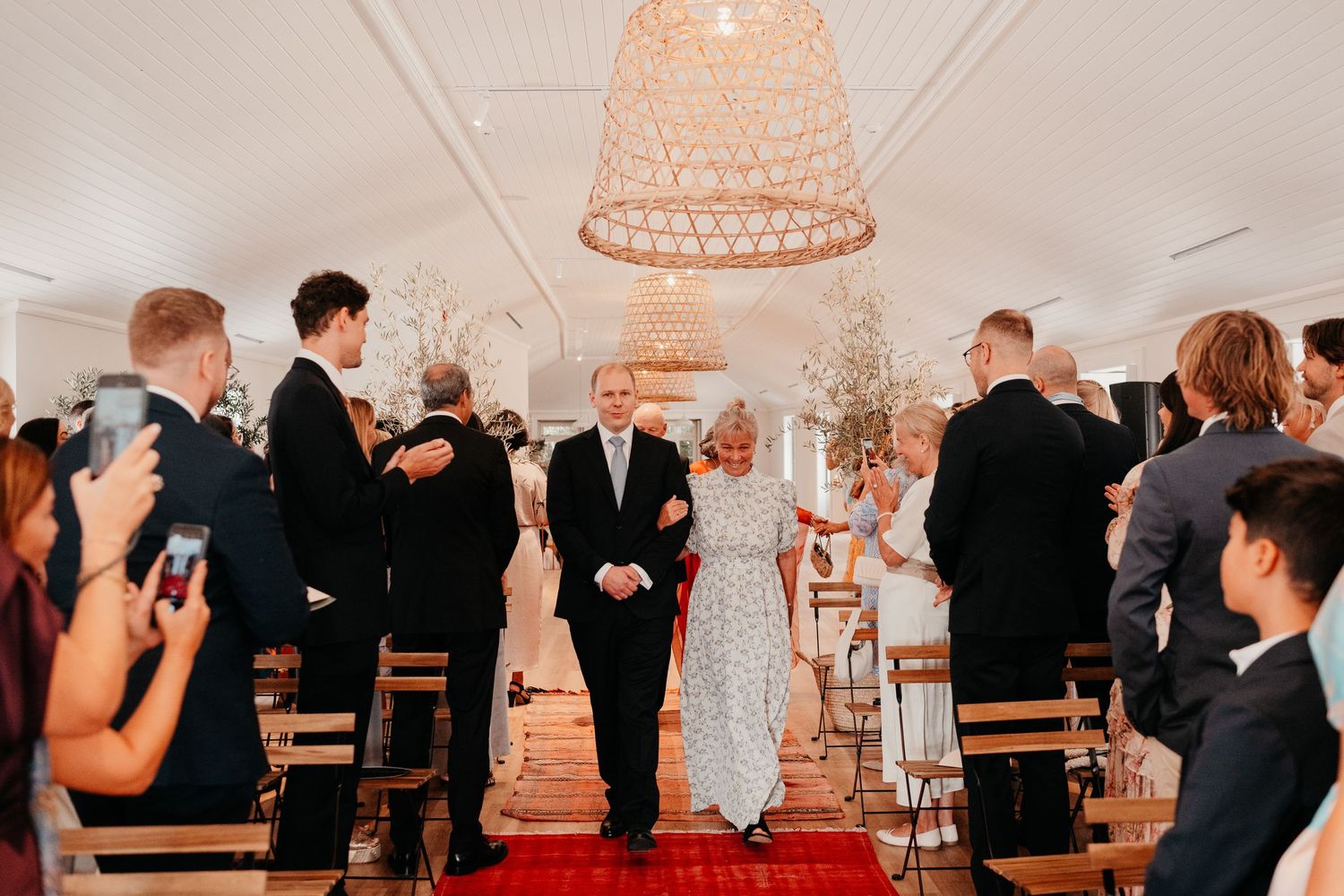Bride and groom walk down the aisle at an elegant wedding ceremony with guests lining the red carpet.