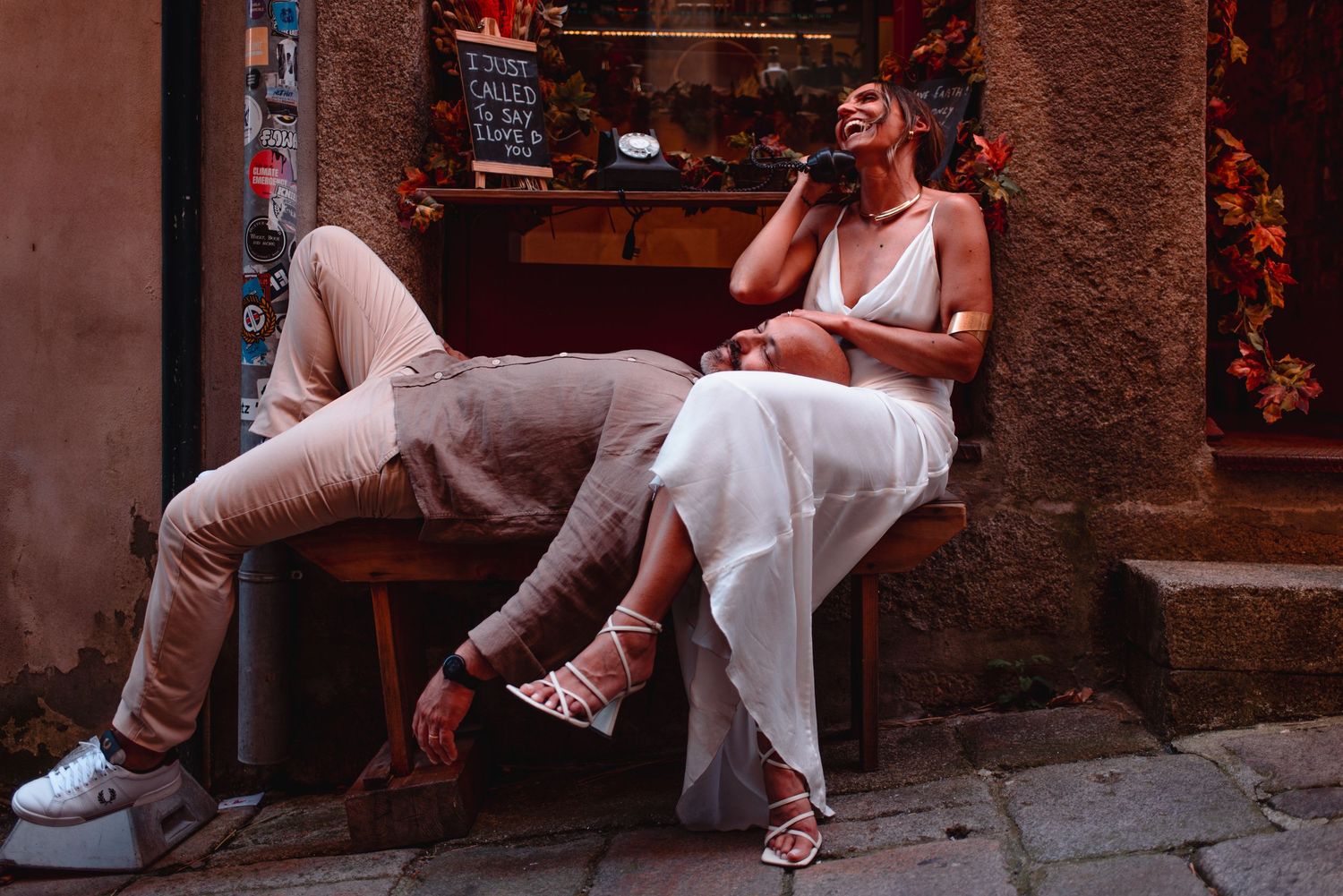 Two people in white outfits share a casual moment on stone steps in an urban setting.