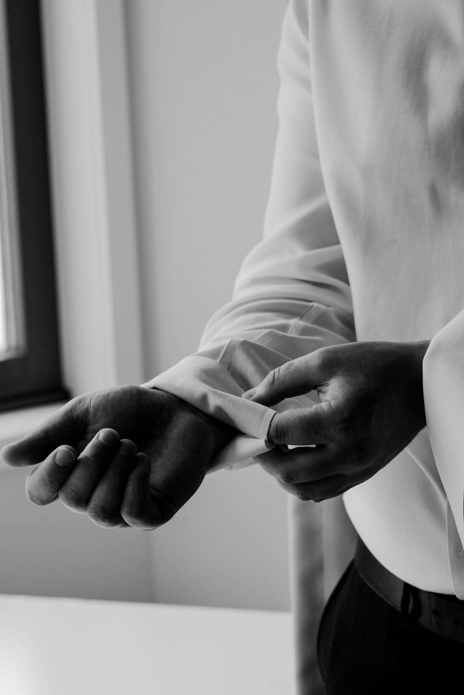 Black and white photo of a groom fastening his cufflinks while dressing for his wedding ceremony.