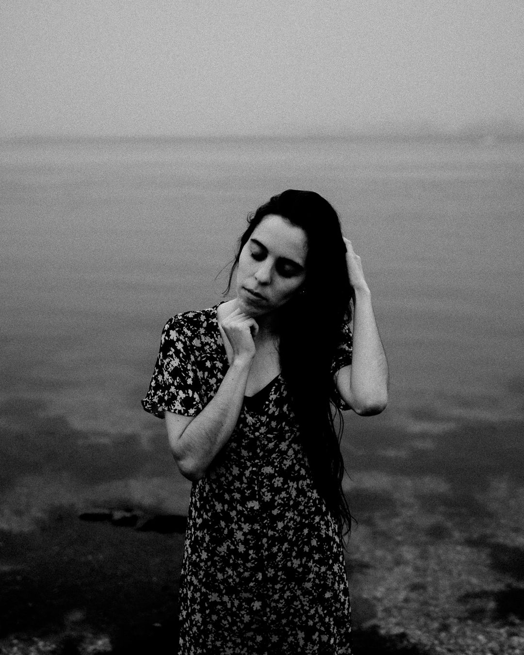 Artistic monochrome portrait showing a person in a floral dress against a serene waterscape.