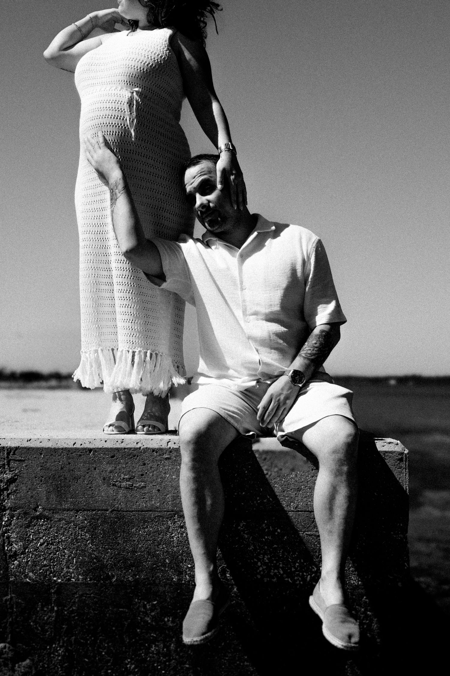 Artistic black and white photo of couple in white attire on concrete ledge.