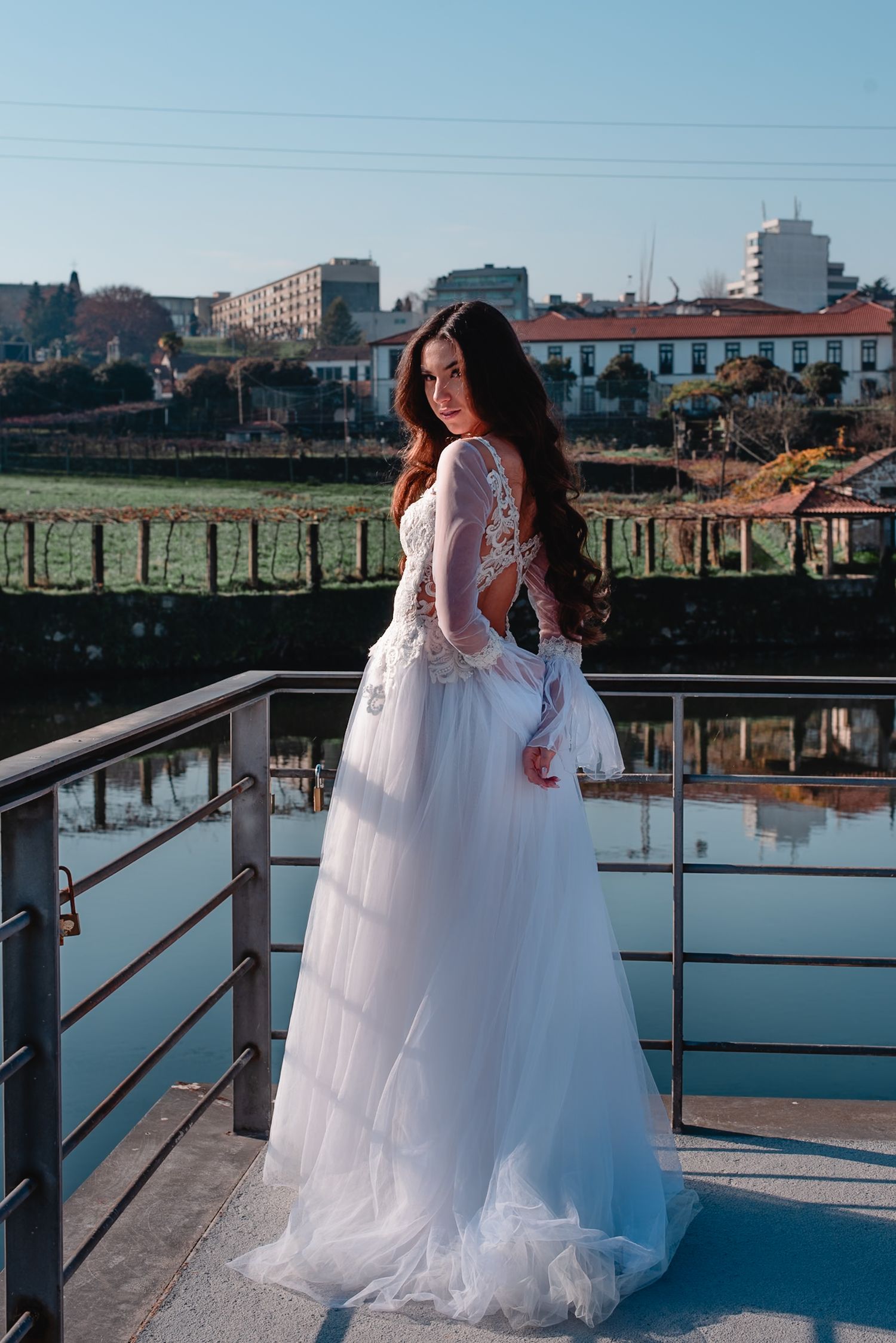 A flowing white wedding dress captured against a serene waterfront backdrop on a sunny day.