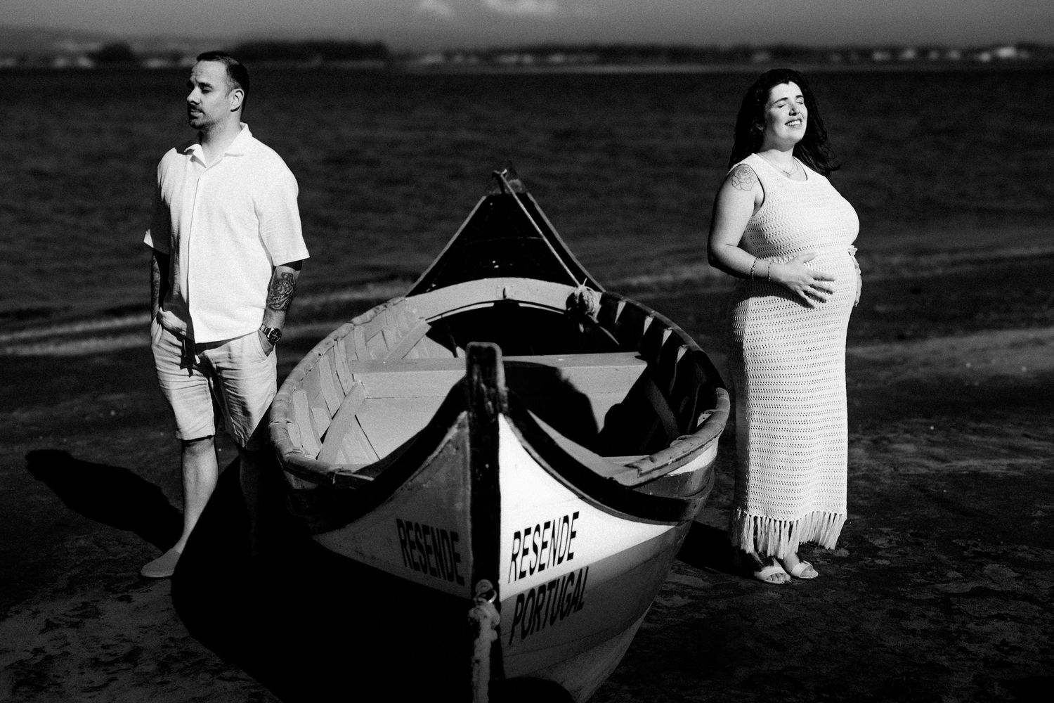 Couple poses with vintage canoe on beach during black and white photoshoot.