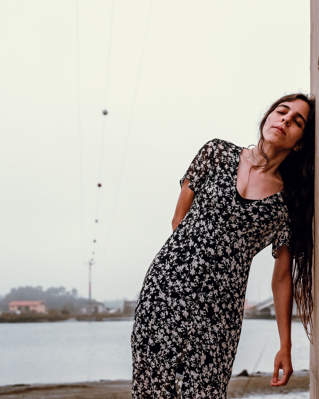 A dreamy pose against a light wall wearing a floral dress near the waterfront.