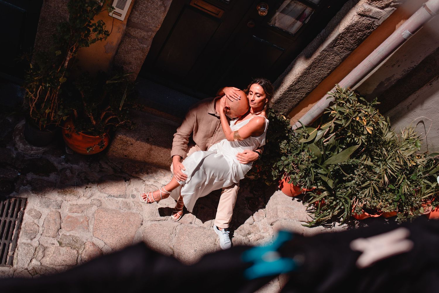 Sunlight creates dramatic shadows in a narrow cobblestone alley during an intimate photoshoot.