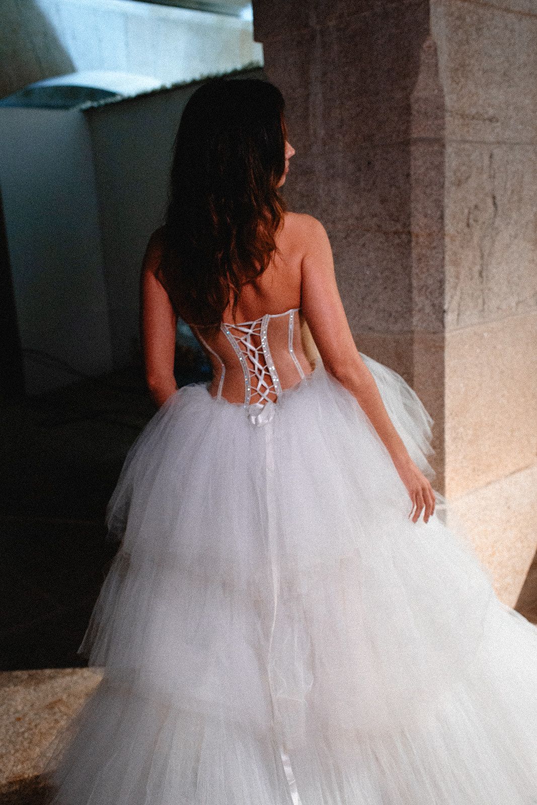 A princess-style wedding dress with intricate back details and layers of tulle photographed indoors.