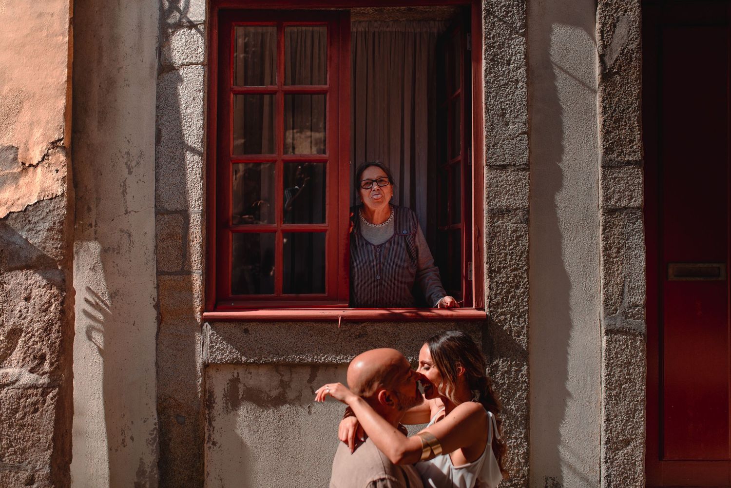 An atmospheric portrait session takes place beside red-framed windows on a textured stone wall.