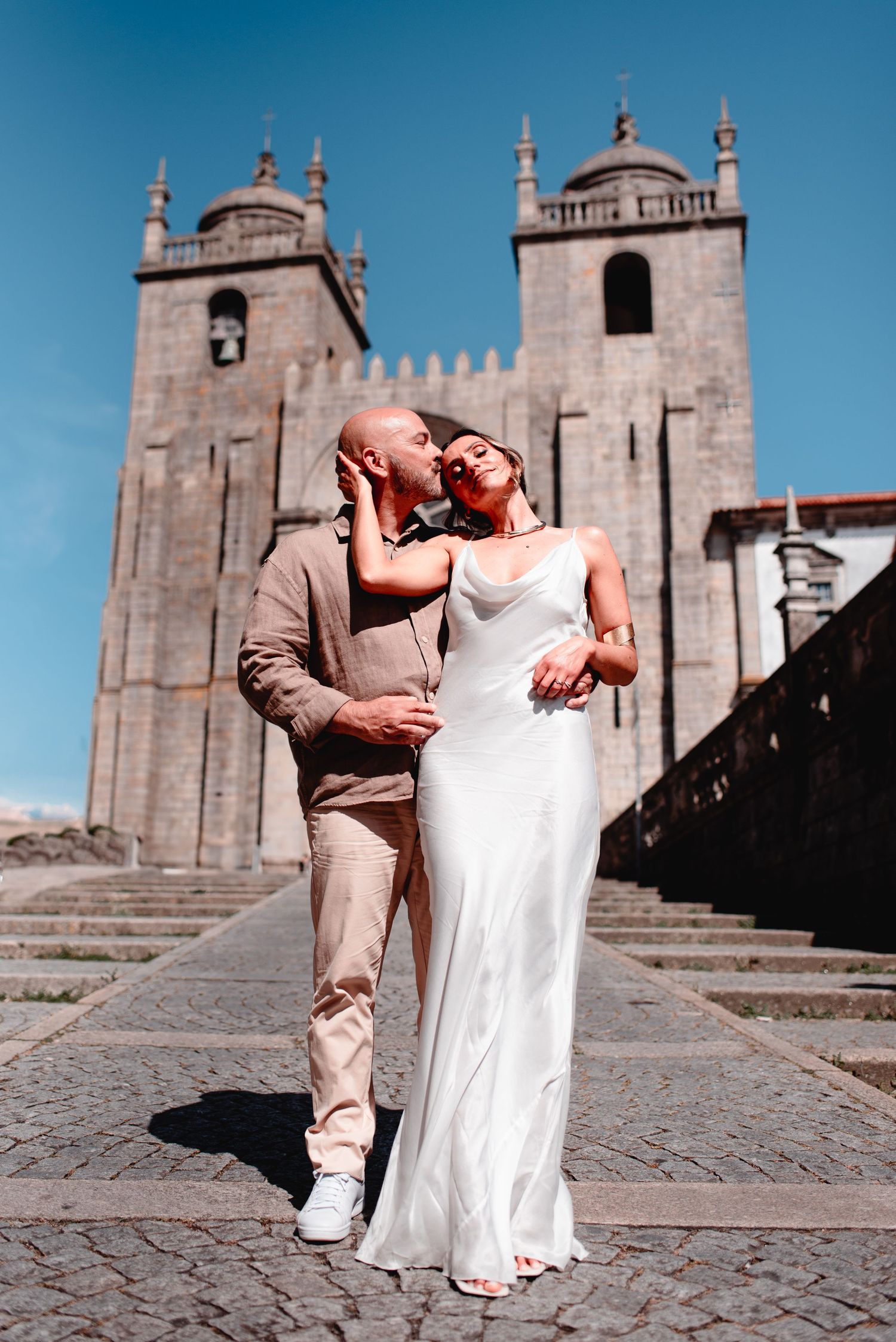 Romantic couple embraces outside historic stone cathedral on cobblestone square.