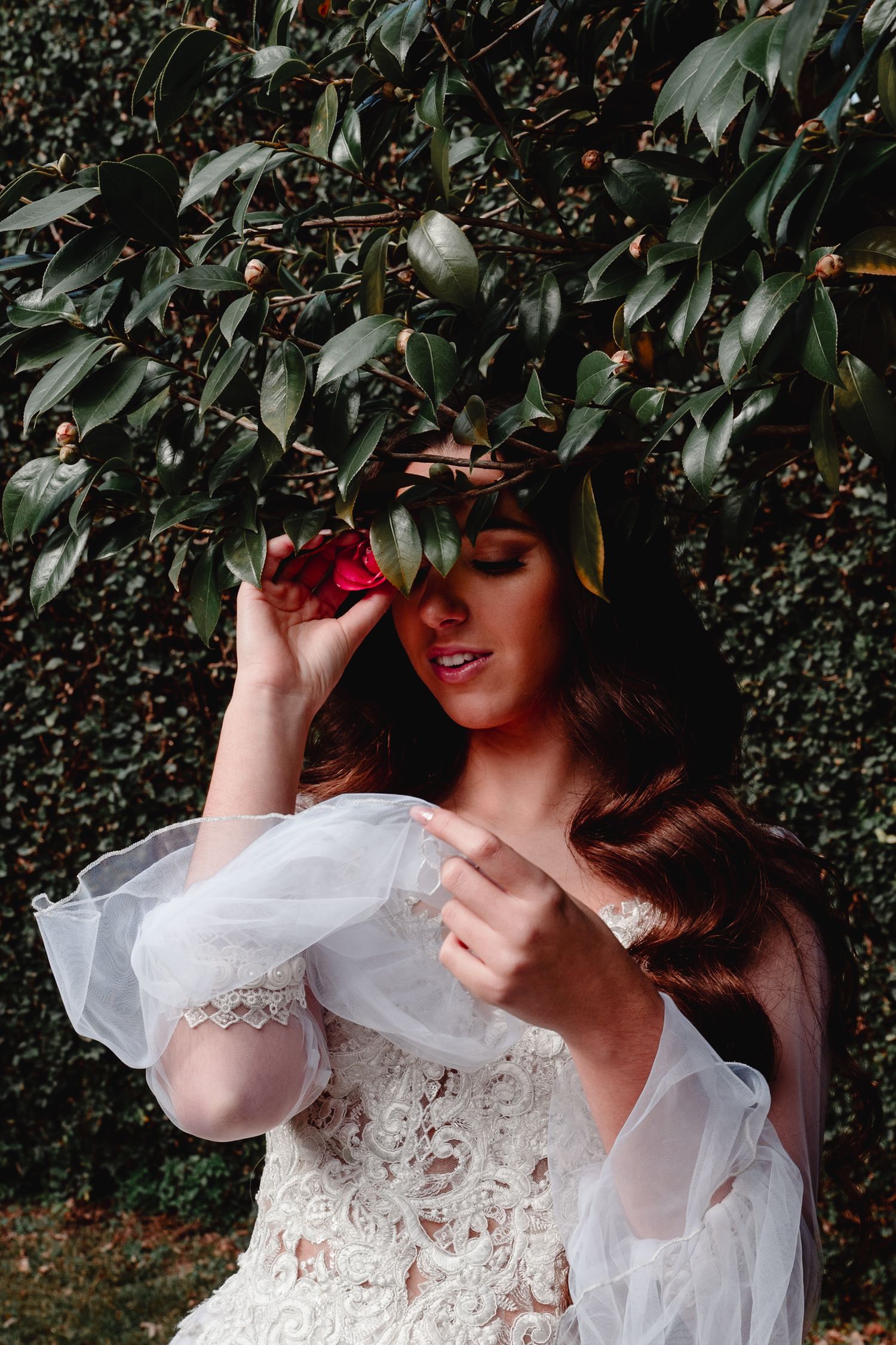 Dreamy bridal portrait amidst lush foliage showcasing a white lace gown and flowing fabric.