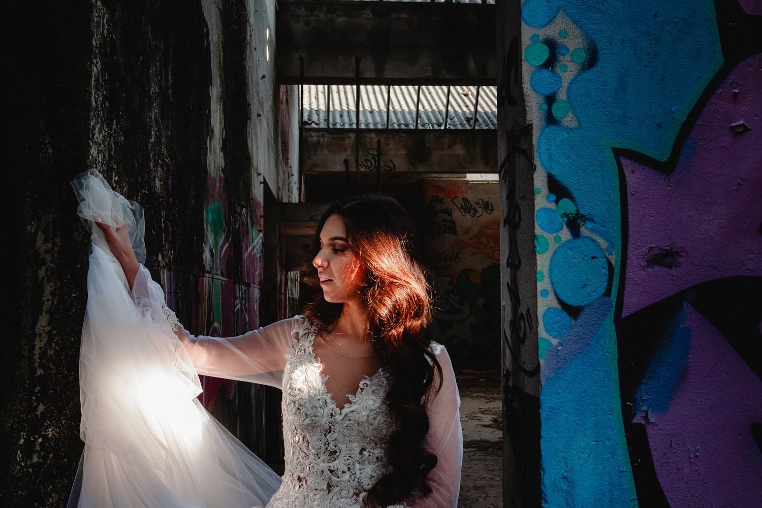 Figure in white dress photographed against urban graffiti wall in dramatic lighting.