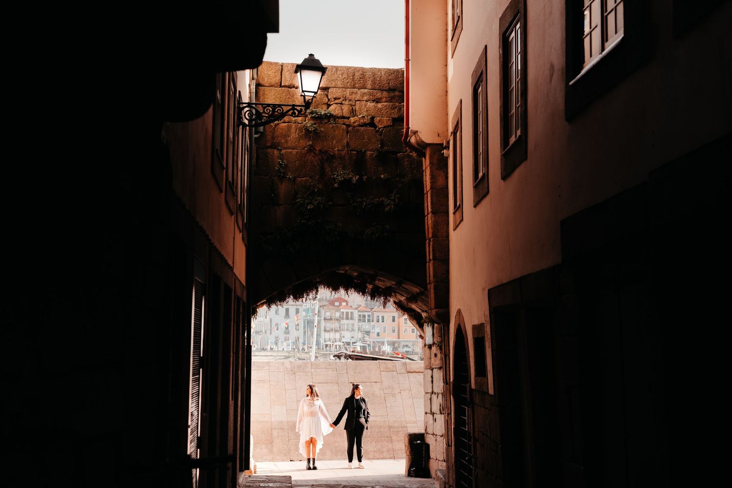 Couple holding hands walking through a romantic cobblestone archway passage in an old European city.