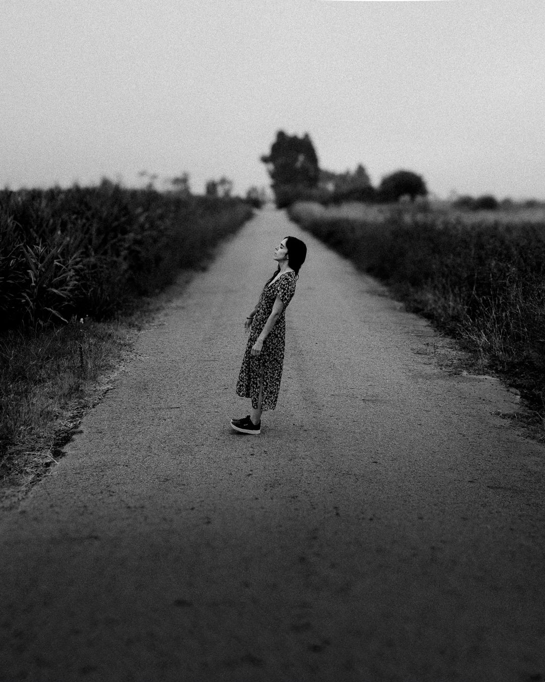 Artistic black and white photo of figure standing on empty rural road.