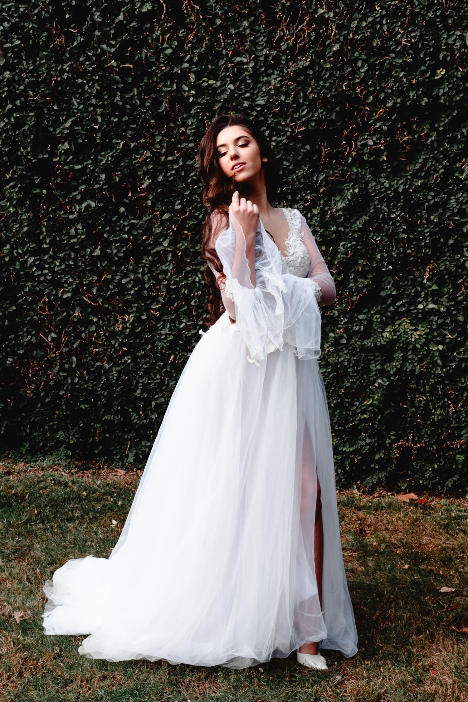 Romantic bridal portrait in flowing white gown against ivy wall backdrop.