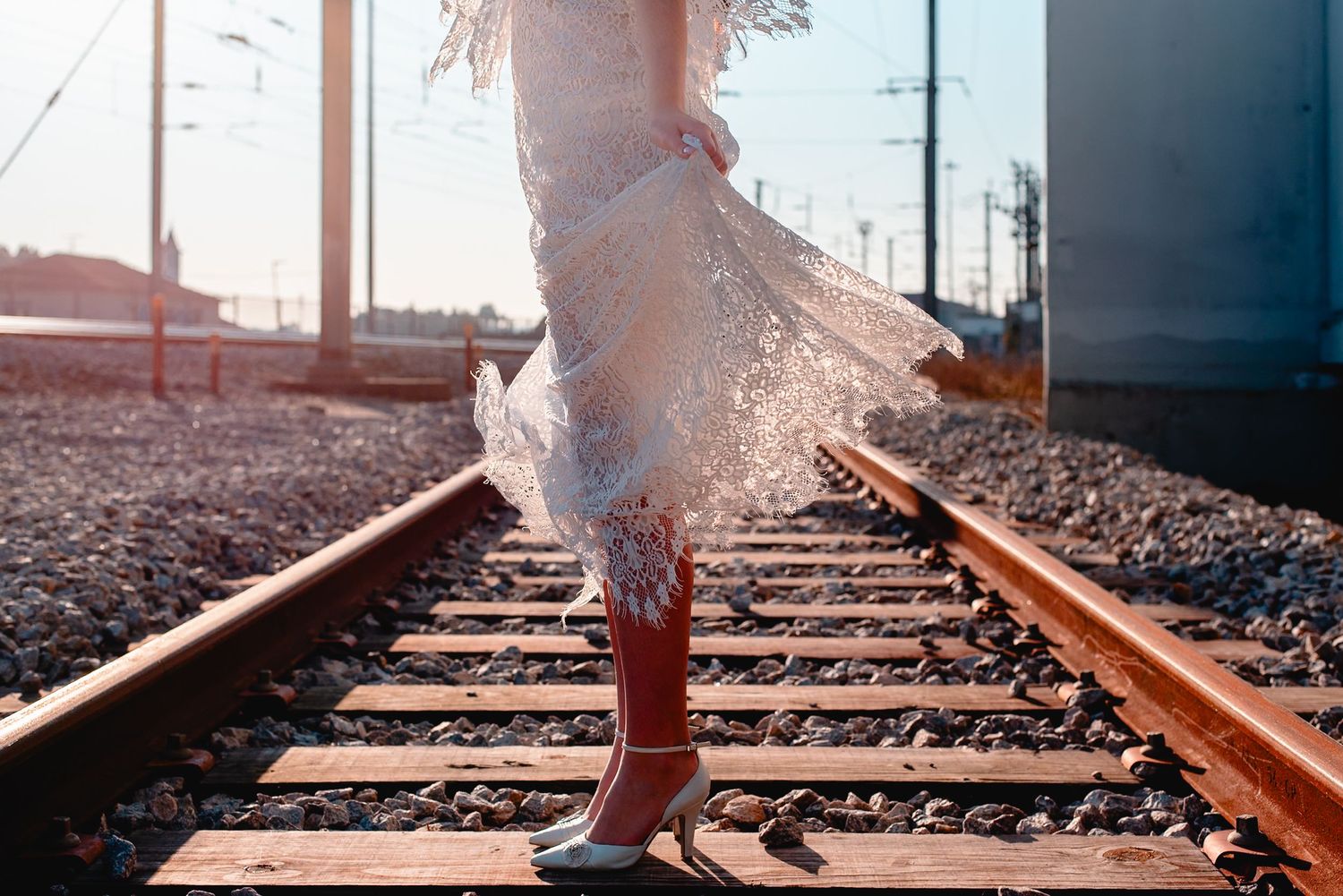 Person in flowing white dress poses dramatically on train tracks during golden hour.