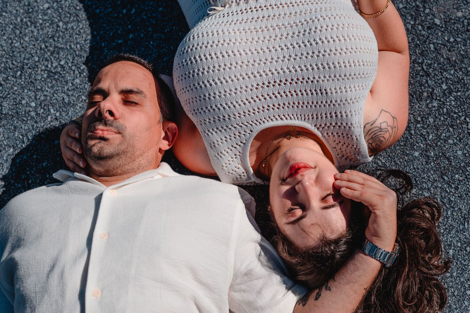 Couple lying together on dark textured surface in artistic pose.