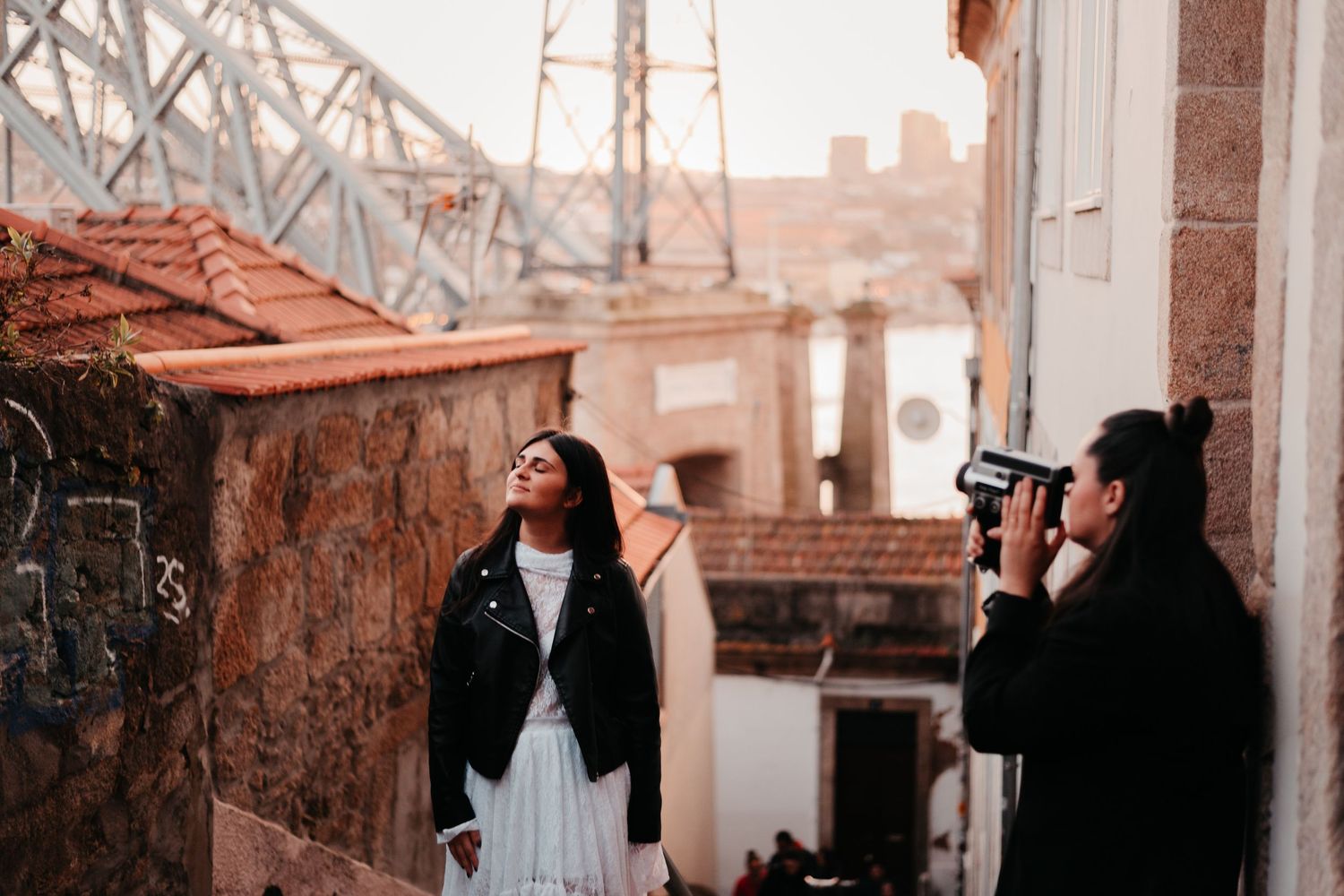 Photographer capturing a woman posing in a narrow alley with historic buildings and a bridge in the background.